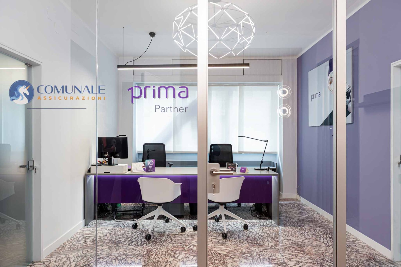 Sala meeting ufficio Comunale Srl Bari con vetrina trasparente logo Comunale Assicurazioni e Prima Partner, scrivania viola con sedute moderne